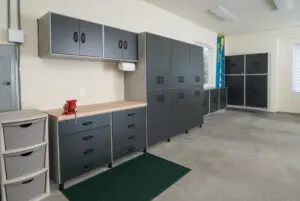 A clean, organized garage with grey storage cabinets, drawers, and a green mat