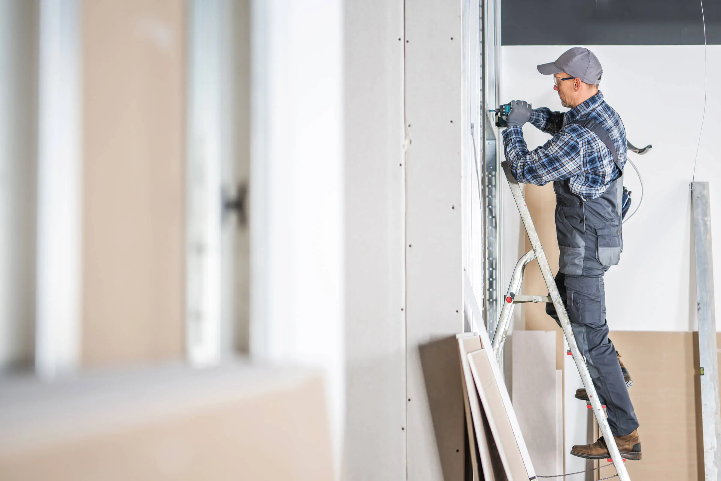 A worker using a power tool to cut drywall in a room under construction or renovation.