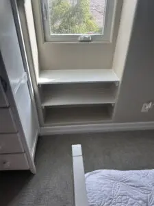 Window with white shelves and quilted bed.